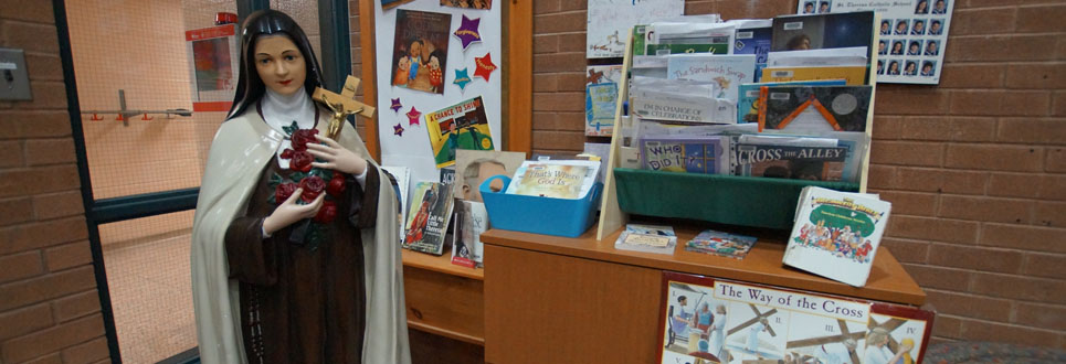 St. Theresa statue beside an desk with educational religious materials.